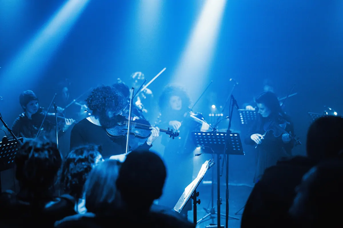 Violinisti Crnogorskog orkestra mladih u plavim snopovima svjetla, publika u prvom planu