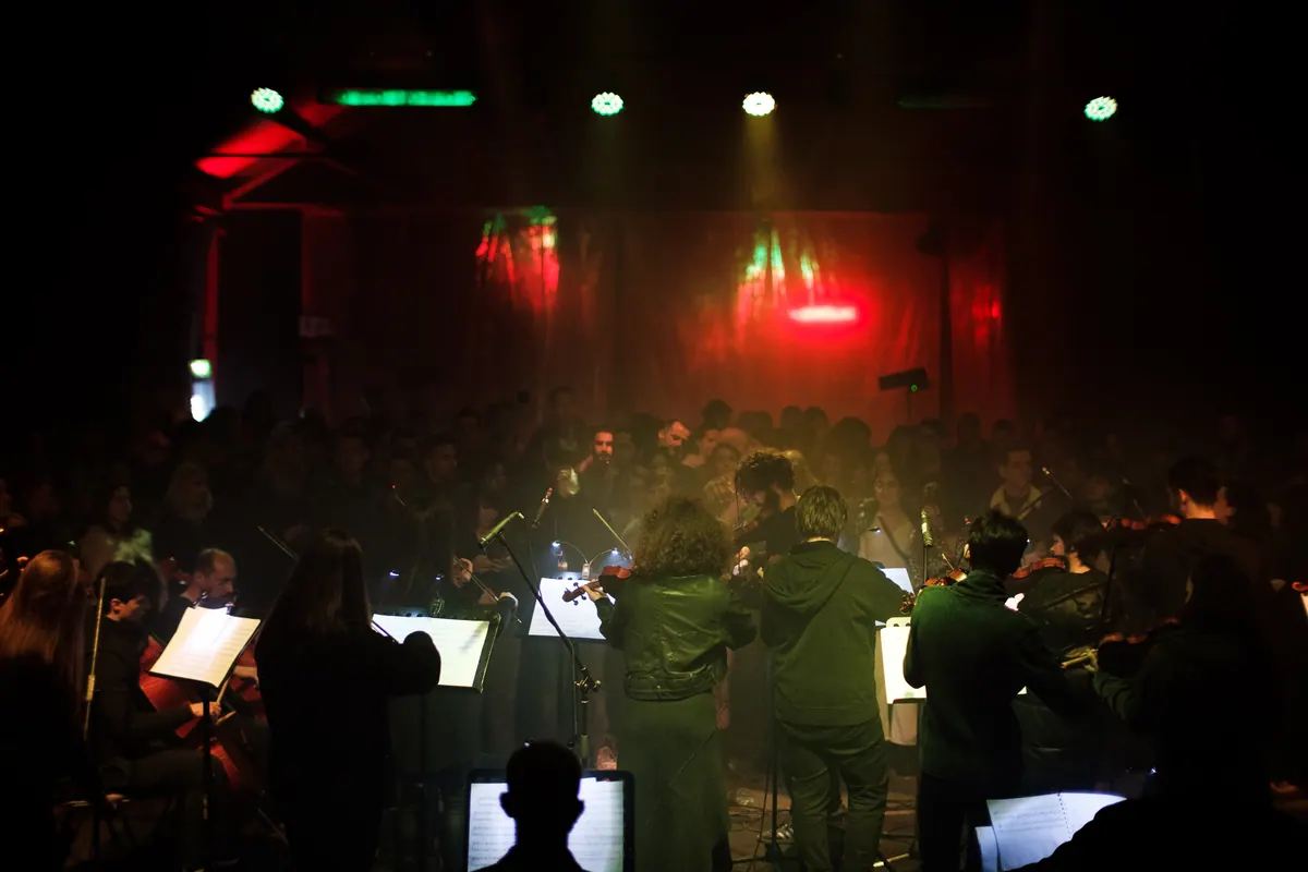 Crnogorski orkestar mladih svira usred publike u hangaru, crveno i zeleno svjetlo