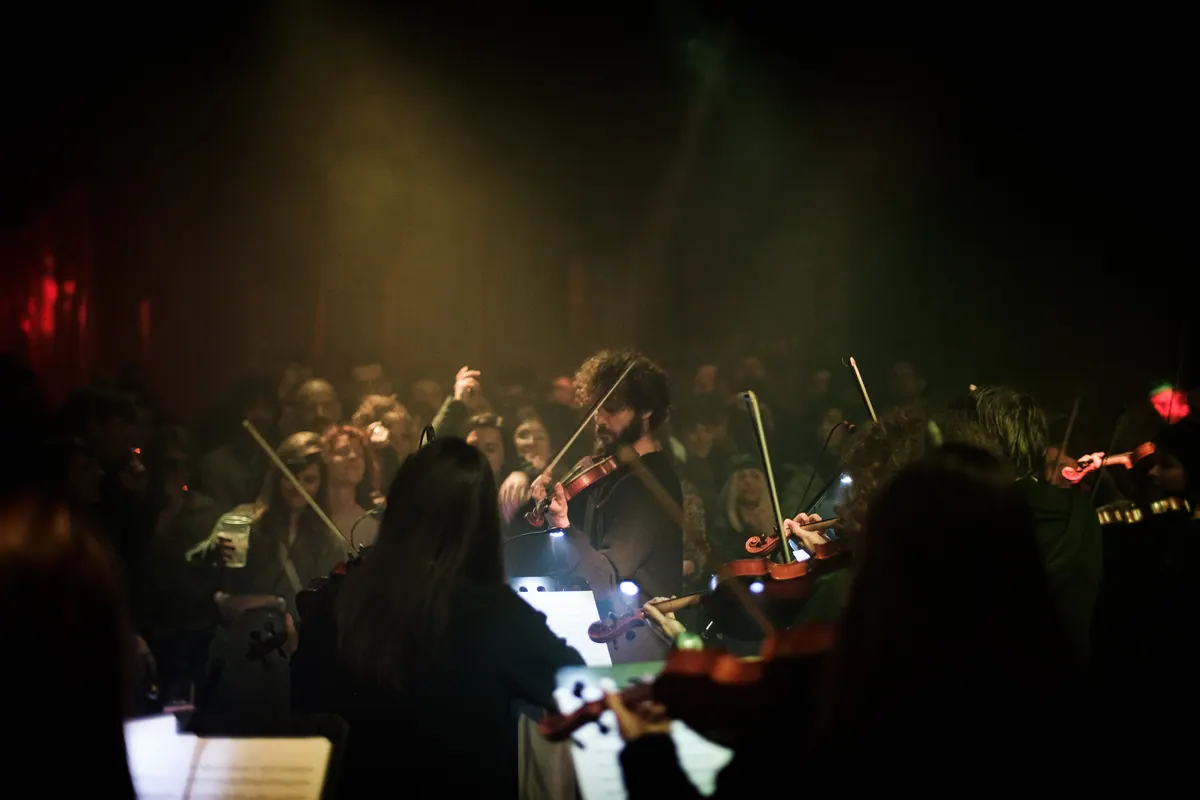 Violinisti sviraju između ljudi, toplo prigušeno svjetlo