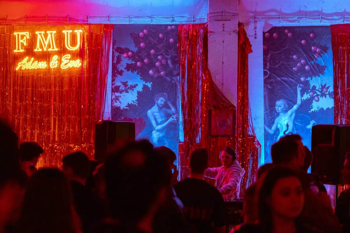 DJ u roze naočarima pred crvenim šljokičastim zavjesama i neonom „FMU Adam & Eva“
