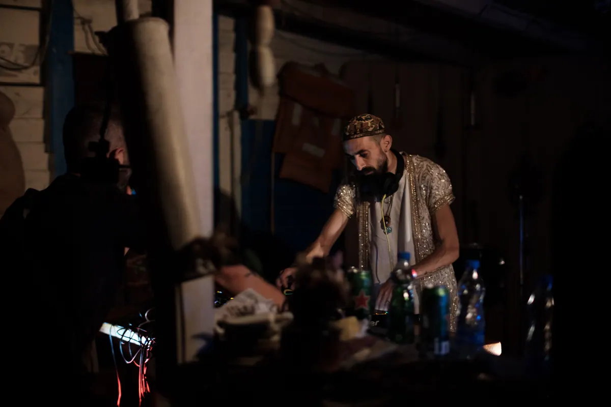 Bradati DJ u šljokičastoj jakni i vezenoj kapi u mraku