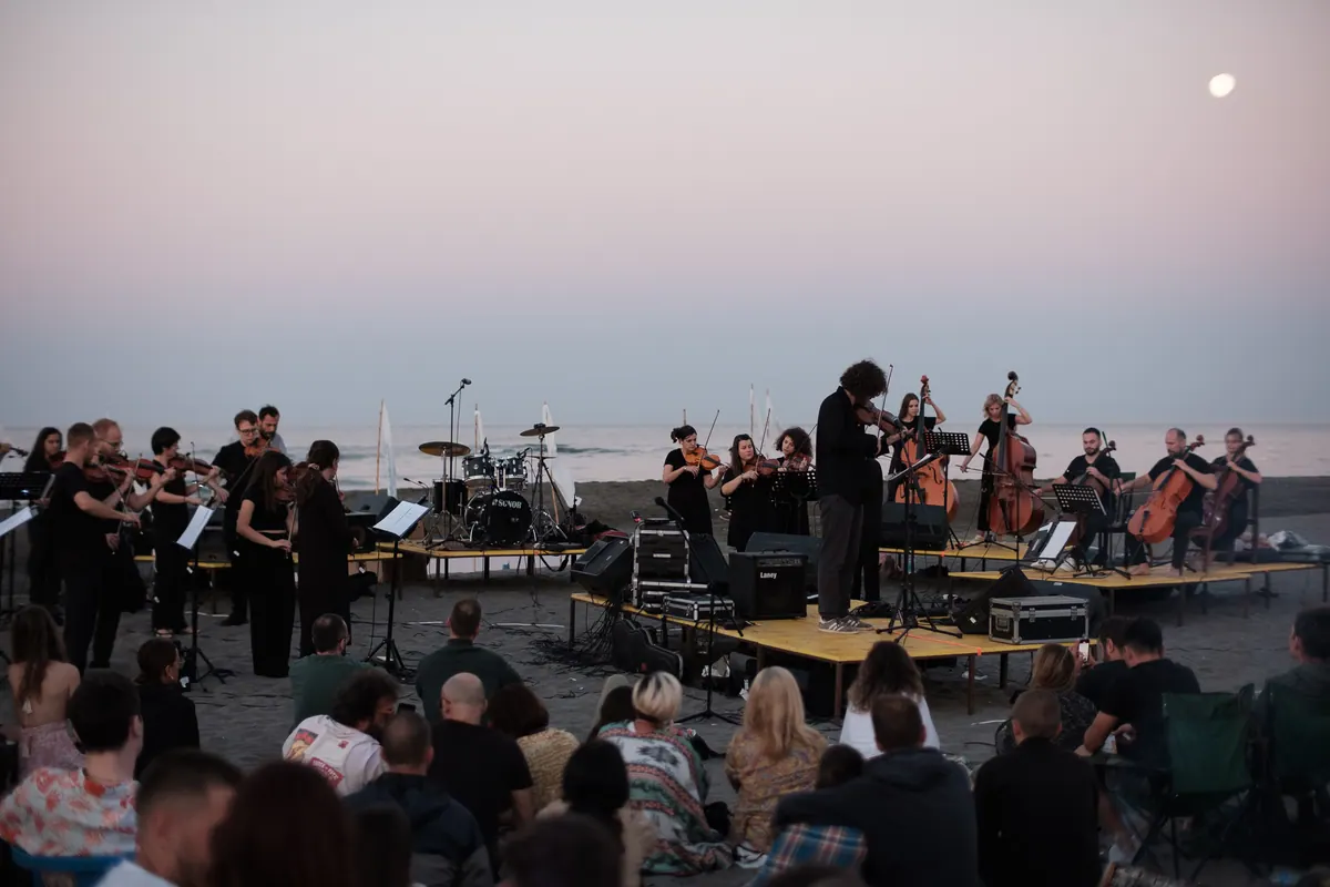 Crnogorski orkestar mladih na drvenim podijumima na pijesku Velike plaže, iza more i mjesec, publika sjedi na pijesku u svitanje