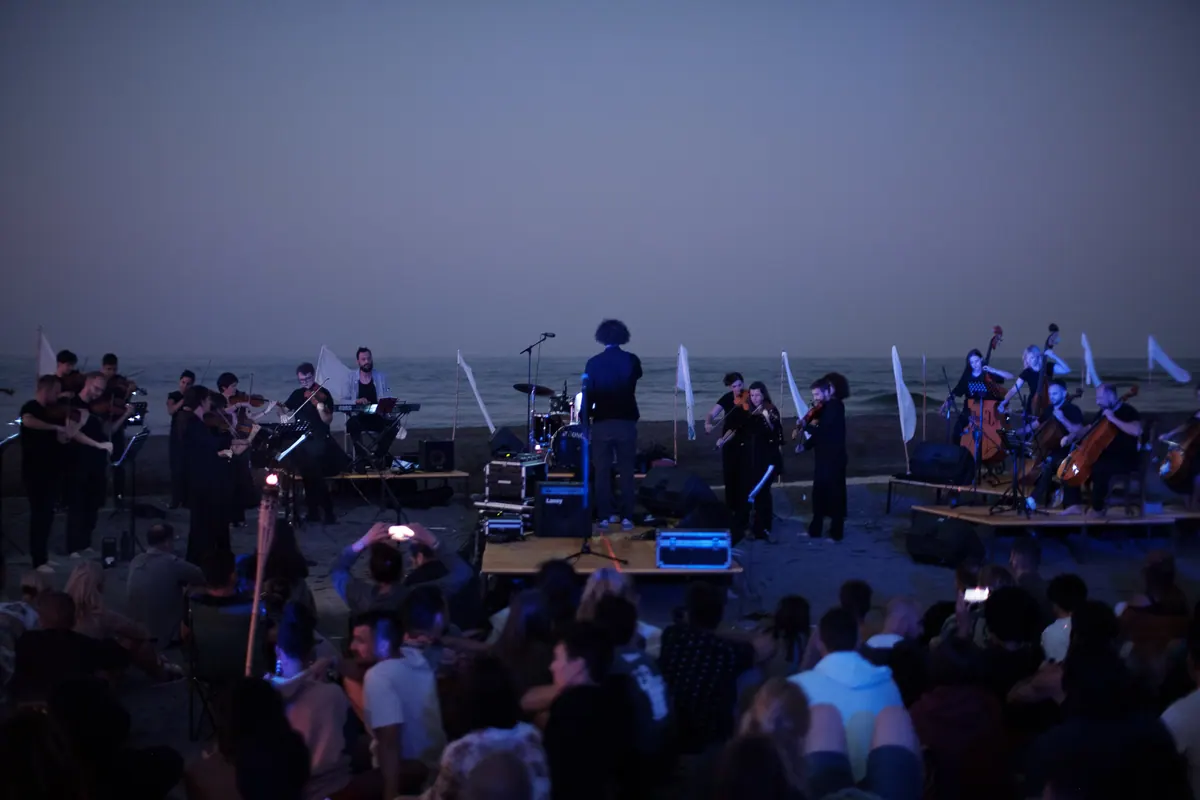 Orkestar u plavi sat pred morem, bijele zastave i publika